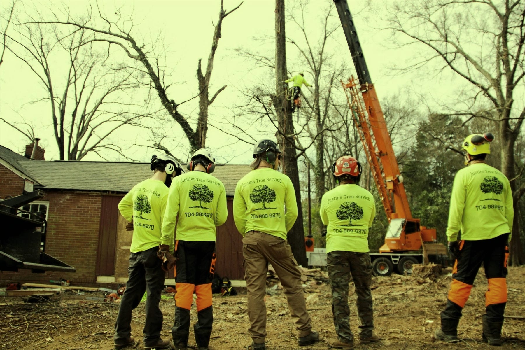 Five crew members in hi-vis shirts and helmets standing together at a job site with an orange crane